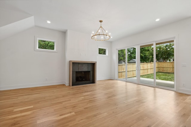 unfurnished living room featuring a tiled fireplace, light hardwood / wood-style flooring, a chandelier, and a healthy amount of sunlight