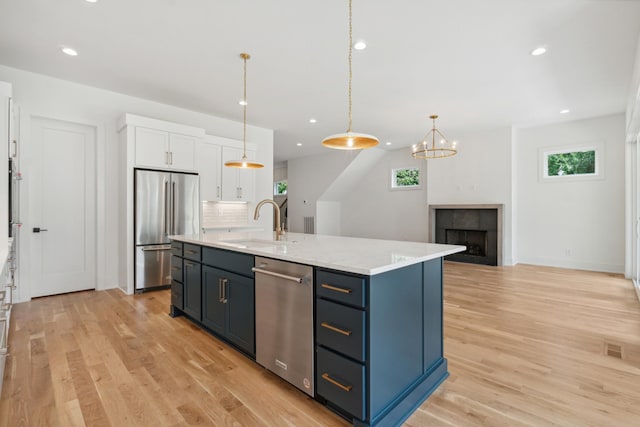 kitchen featuring sink, appliances with stainless steel finishes, white cabinetry, an island with sink, and decorative light fixtures