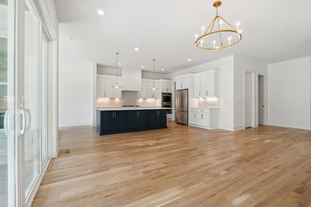 kitchen featuring white cabinetry, hanging light fixtures, light hardwood / wood-style flooring, appliances with stainless steel finishes, and a kitchen island with sink