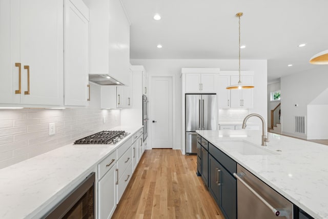 kitchen featuring wall chimney exhaust hood, sink, appliances with stainless steel finishes, pendant lighting, and white cabinets