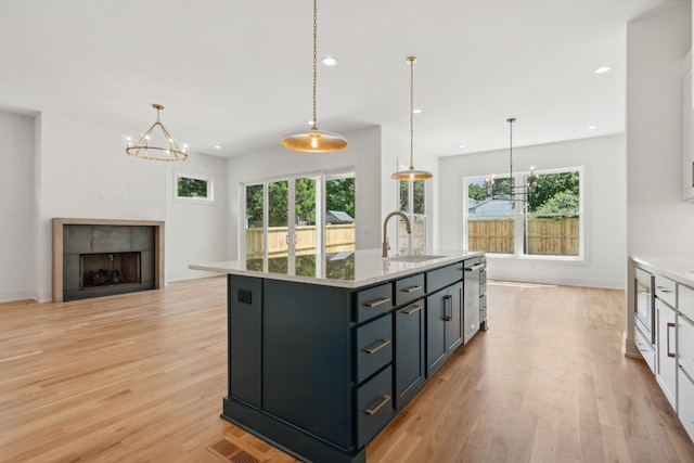 kitchen featuring a kitchen island with sink, sink, pendant lighting, and white cabinets