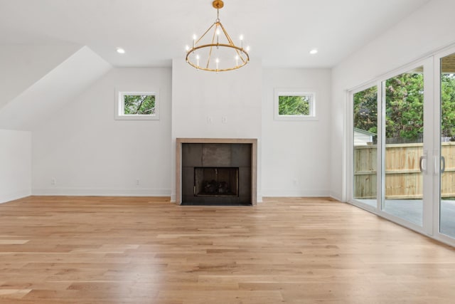 unfurnished living room featuring lofted ceiling, a healthy amount of sunlight, a tiled fireplace, and light hardwood / wood-style flooring