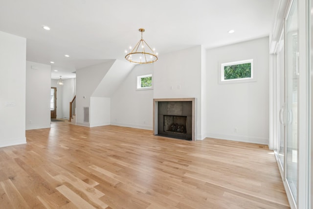 unfurnished living room featuring an inviting chandelier, a tiled fireplace, and light hardwood / wood-style floors