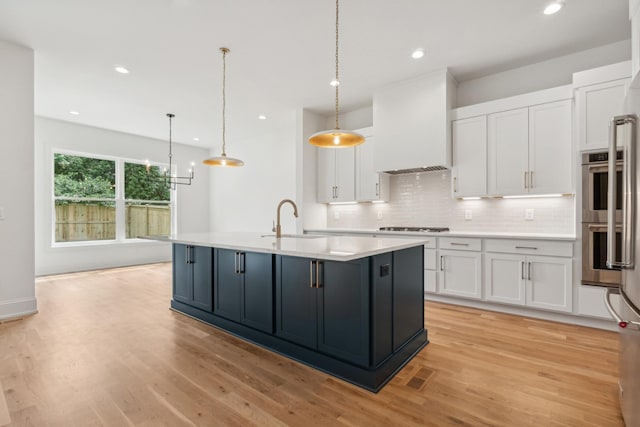 kitchen featuring custom exhaust hood, white cabinetry, a kitchen island with sink, and pendant lighting