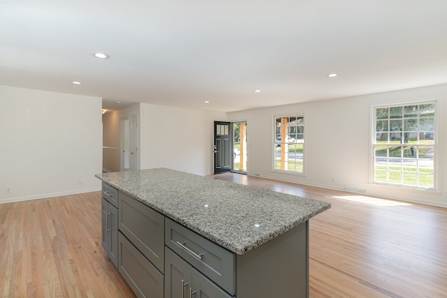 kitchen with light wood-type flooring, a healthy amount of sunlight, a center island, and light stone countertops