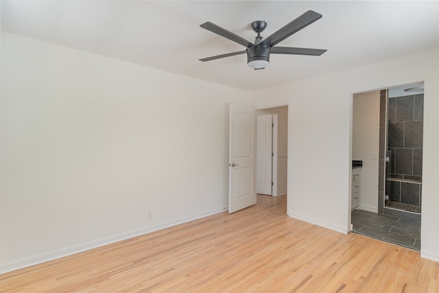 unfurnished bedroom with ceiling fan, ensuite bathroom, a tile fireplace, and light hardwood / wood-style floors