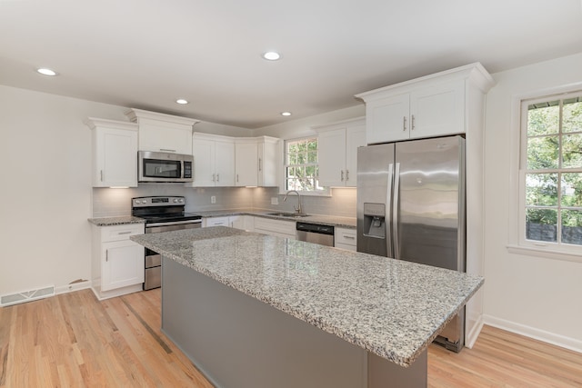 kitchen with appliances with stainless steel finishes, white cabinetry, backsplash, light stone counters, and light hardwood / wood-style flooring