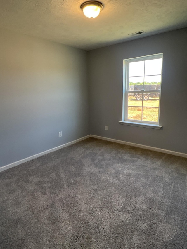 empty room featuring dark colored carpet, visible vents, and baseboards