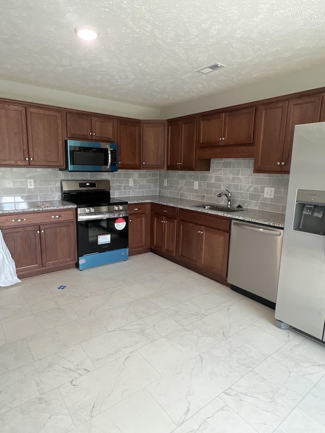 kitchen with marble finish floor, backsplash, appliances with stainless steel finishes, a sink, and light stone countertops