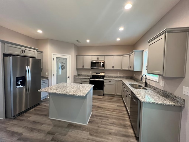 kitchen with dark wood-style floors, a kitchen island, gray cabinets, a sink, and appliances with stainless steel finishes