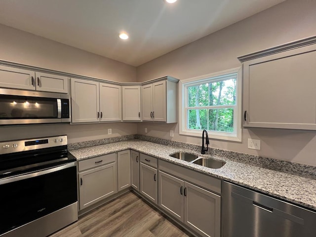 kitchen with gray cabinets, a sink, wood finished floors, appliances with stainless steel finishes, and lofted ceiling