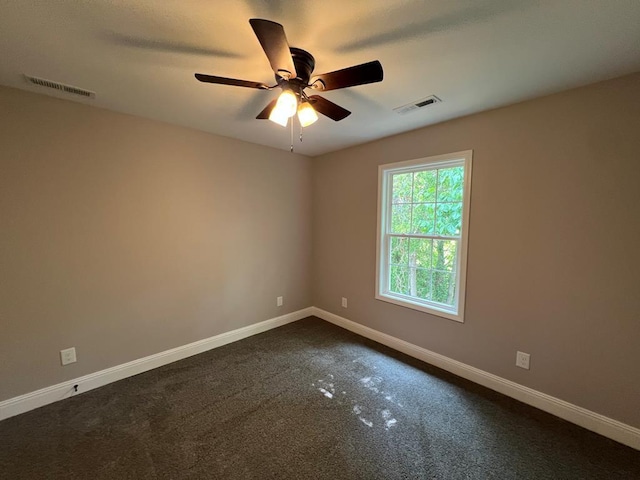 spare room featuring dark colored carpet, visible vents, baseboards, and ceiling fan