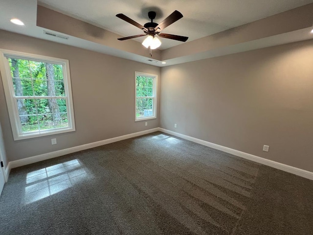 unfurnished room featuring visible vents, baseboards, dark carpet, a raised ceiling, and a ceiling fan