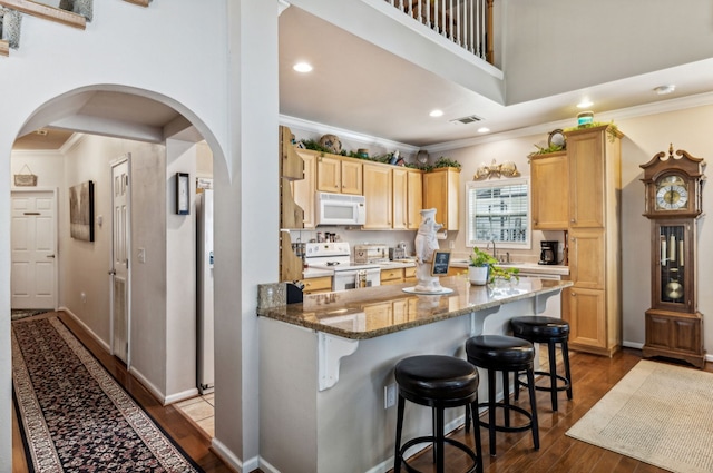 kitchen featuring white appliances, light brown cabinets, hardwood / wood-style flooring, dark stone counters, and sink