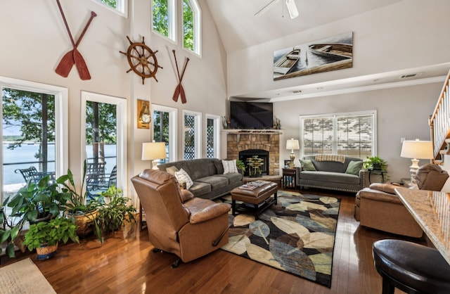 living room with high vaulted ceiling, a stone fireplace, wood-type flooring, and a healthy amount of sunlight