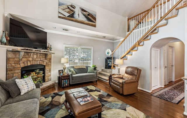 living room featuring hardwood / wood-style floors, a fireplace, ornamental molding, and a high ceiling