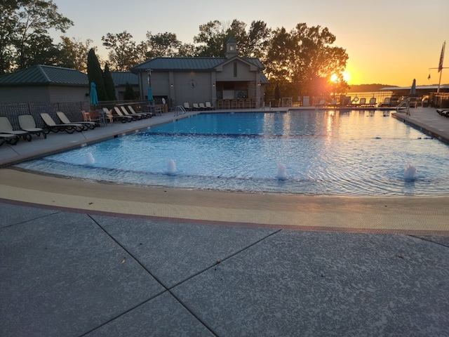 pool at dusk featuring pool water feature and a patio