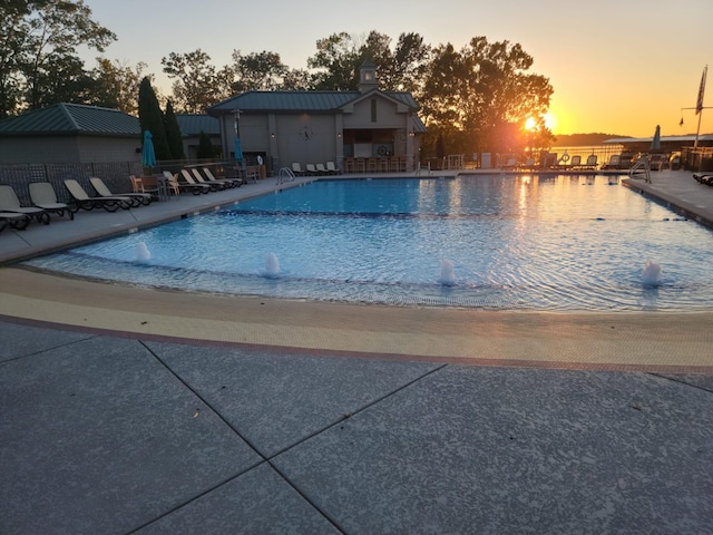 pool at dusk featuring a patio area and a community pool