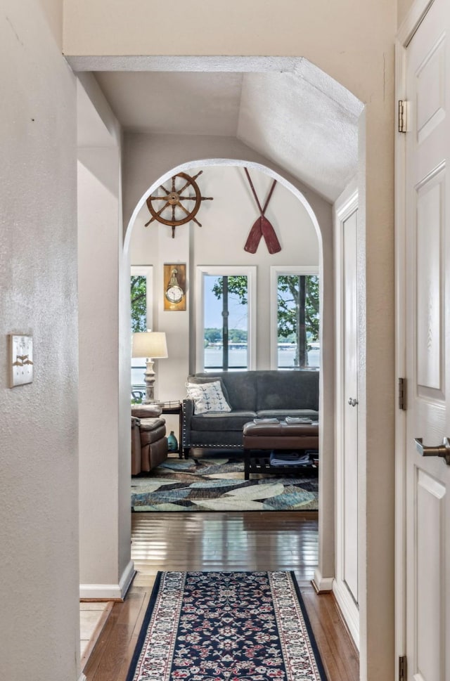 hall featuring vaulted ceiling, arched walkways, hardwood / wood-style flooring, and baseboards