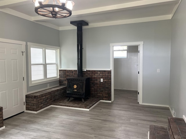 unfurnished living room with hardwood / wood-style flooring, beamed ceiling, a notable chandelier, and a wood stove