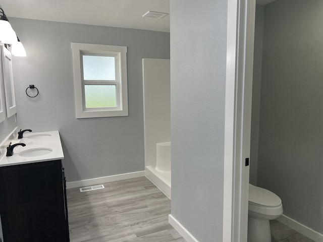 bathroom featuring double sink vanity, walk in shower, hardwood / wood-style flooring, and toilet