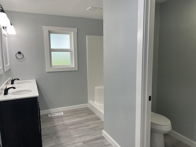 bathroom featuring hardwood / wood-style flooring, vanity, a shower, and toilet