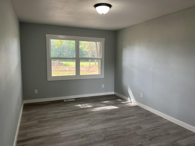 empty room with dark hardwood / wood-style flooring and a textured ceiling