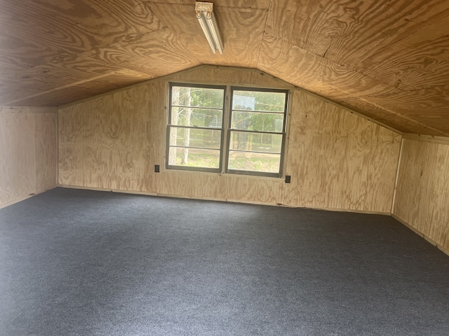 additional living space with wood walls, dark carpet, and vaulted ceiling