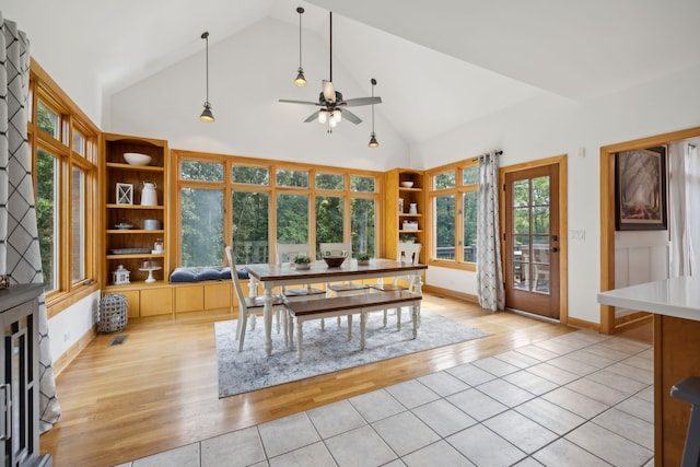 dining room with ceiling fan, high vaulted ceiling, built in shelves, and light hardwood / wood-style floors