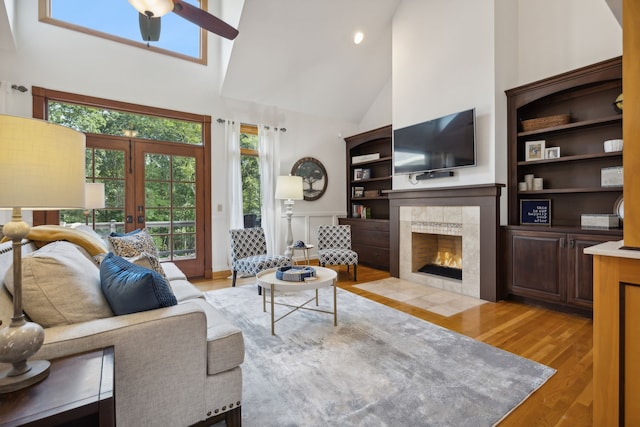 living room with built in shelves, high vaulted ceiling, ceiling fan, a tile fireplace, and light hardwood / wood-style flooring