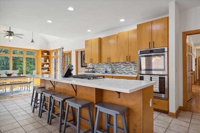 kitchen with light tile patterned floors, appliances with stainless steel finishes, a kitchen bar, backsplash, and sink