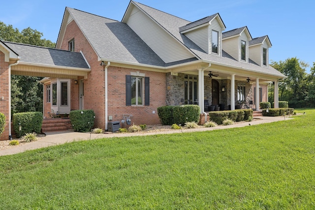 cape cod house with brick siding, roof with shingles, a porch, a front yard, and ceiling fan