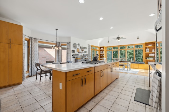 kitchen with ceiling fan with notable chandelier, stainless steel gas stovetop, light tile patterned floors, a center island, and decorative light fixtures