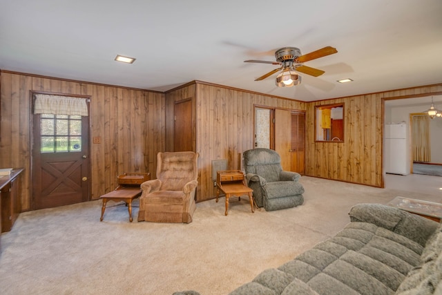 carpeted living room featuring ceiling fan, wood walls, and crown molding