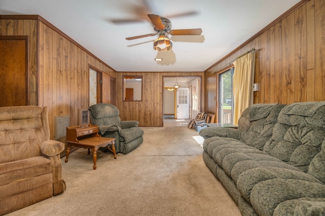 carpeted living room with wood walls, crown molding, and ceiling fan