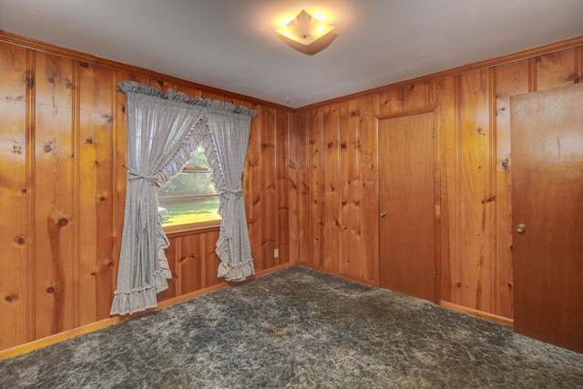 unfurnished room featuring crown molding, wooden walls, and carpet floors