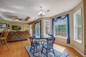 dining space featuring light wood-type flooring, a raised ceiling, and ceiling fan with notable chandelier