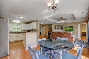 dining room featuring sink, a tray ceiling, ceiling fan with notable chandelier, and light hardwood / wood-style floors