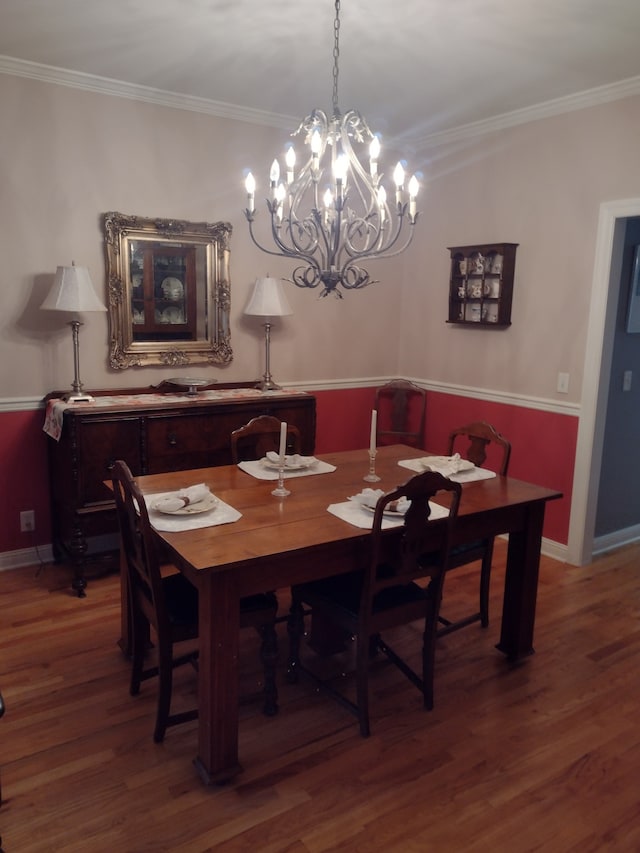 dining area with wood-type flooring, ornamental molding, and an inviting chandelier