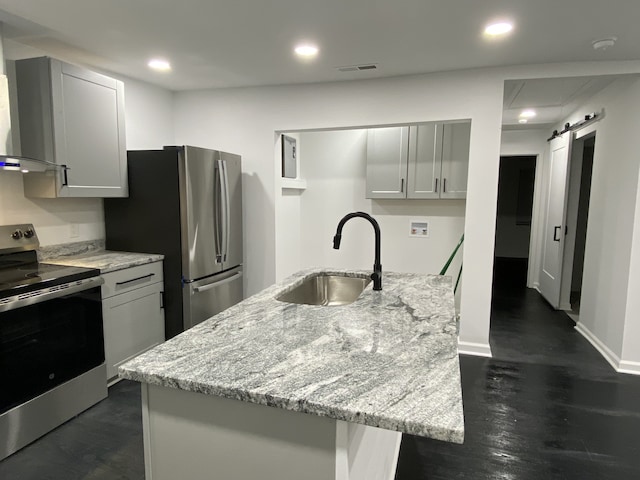 kitchen with light stone countertops, sink, stainless steel appliances, a barn door, and an island with sink