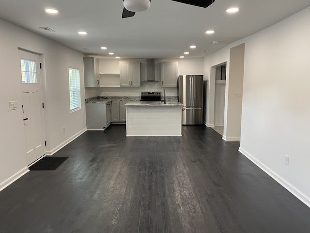 kitchen featuring light stone countertops, dark wood-type flooring, stainless steel appliances, wall chimney range hood, and a kitchen island