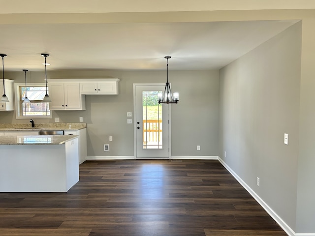 kitchen featuring light stone countertops, dark hardwood / wood-style flooring, stainless steel dishwasher, pendant lighting, and white cabinetry