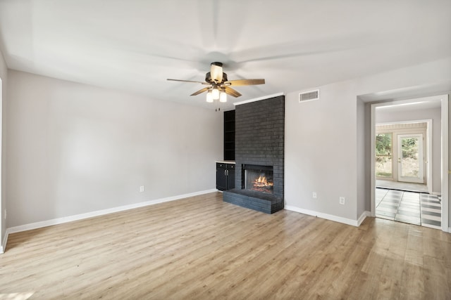 unfurnished living room with ceiling fan, brick wall, light wood-type flooring, and a brick fireplace