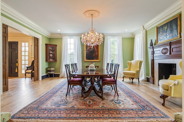 dining room with a notable chandelier, light hardwood / wood-style flooring, ornamental molding, and a high end fireplace