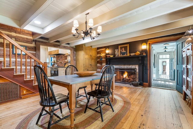 dining space with light hardwood / wood-style flooring, a stone fireplace, an inviting chandelier, and beamed ceiling