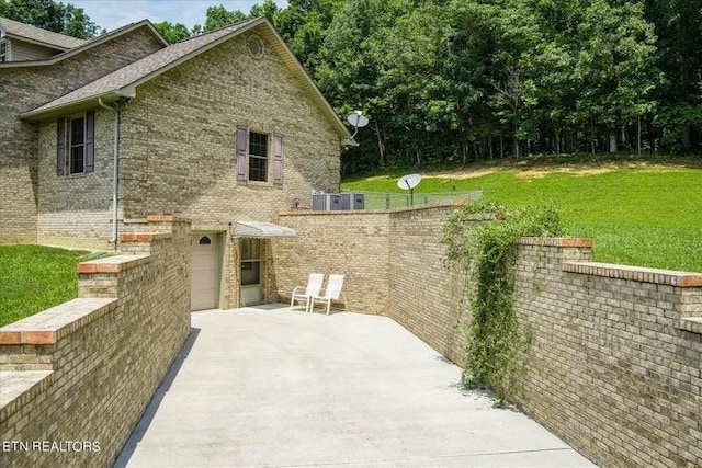 view of side of home featuring a garage, brick siding, driveway, a yard, and a patio area