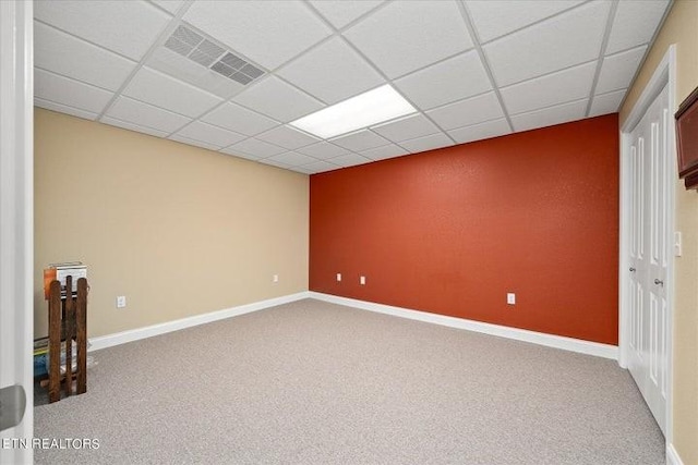 carpeted empty room with a paneled ceiling, visible vents, and baseboards