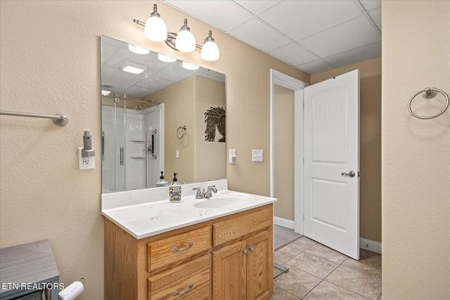 bathroom with a shower, a paneled ceiling, vanity, tile patterned flooring, and baseboards