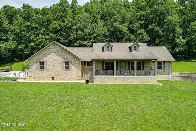 cape cod-style house with covered porch, a front lawn, and a wooded view