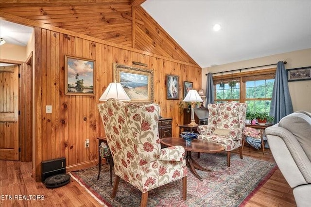 living area featuring vaulted ceiling, wooden walls, and wood finished floors